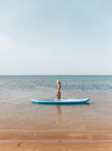 a girl sitting on a surfboard on the beach at Thalassa Beach Family & Waterpark Resort in Vokolidha