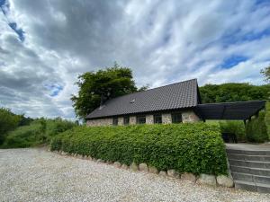 a house with a black roof and a hedge at Stenhuset i Pilbrodalen in Skanderborg