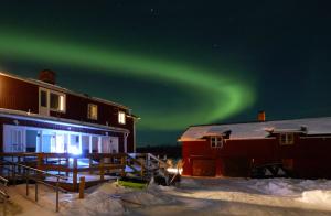 an aurora in the sky over a house and a barn at The Friendly Moose in Övertorneå