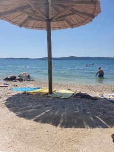 uma praia com um guarda-sol e pessoas na água em Apartments villa M&M em Bibinje