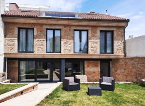 una casa de ladrillo con ventanas negras y sillas en el patio en Solpor do Coído, en Muxía