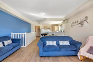 a living room with two blue couches and a kitchen at The Lighthouse - Port Willunga - C21 SouthCoast Holidays in Port Willunga