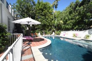 a swimming pool with an umbrella and chairs next to a house at Beverly Hills Celebrity Home in Los Angeles