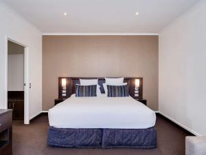 a bedroom with a large white bed with blue pillows at Novotel Rotorua Lakeside in Rotorua