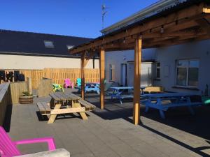 a patio with wooden picnic tables and pink chairs at Rougey Lodge Hostel in Bundoran