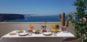 a table with food and drinks and a view of the ocean at Apartment Praia Arrifana with BALCONY and SEA VIEW in Aljezur