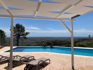a swimming pool with two chairs under a white canopy at B&B Quinta O Ninho in Monchique
