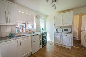 a kitchen with white cabinets and a sink and a stove at The Burrow in Liskeard