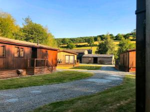 a group of wooden buildings on a gravel road at Alder River Lodge Clun Valley Luxury Hot Tub Break in Craven Arms