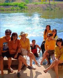 un grupo de personas sentadas en un banco junto al agua en Kaengkrachan River Hut en Kaeng Kachan
