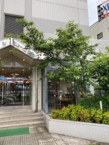 un bâtiment avec un arbre devant un magasin dans l'établissement Hotel New Yutaka, à Izumi-Sano