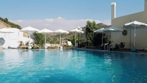 a swimming pool with blue water and white umbrellas at Melissa Hotel in Matala