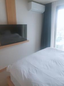 Sokcho Daemyung Heidi Pension في سوكشو: غرفة نوم بسرير ابيض وتلفزيون على الحائط
