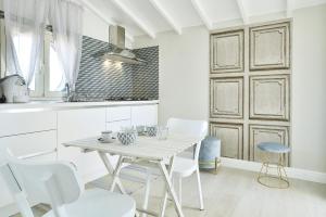 a white kitchen with a table and white chairs at Romantic House Porto Ulisse in Santa Maria Del Focallo
