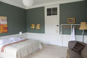 a bedroom with green walls and a bed and a chair at Vemmetofte Pr&aelig;steg&aring;rd in Faxe