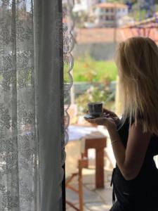 a woman holding a cup of coffee looking out a window at Athina Studios in Chorto