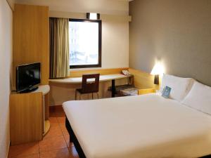 ein Hotelzimmer mit einem Bett, einem Schreibtisch und einem TV in der Unterkunft ibis Santos Gonzaga Praia in Santos