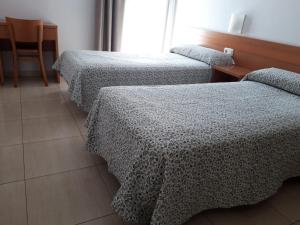 2 Betten in einem Zimmer mit einem Tisch und einem Stuhl in der Unterkunft Hostal Cal Siles in El Prat de Llobregat