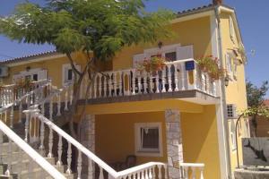 a yellow house with a white balcony and a tree at Apartments Nella in Sveti Anton