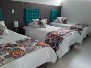3 Betten in einem Hotelzimmer mit bunten Decken in der Unterkunft Hotel Grato Manizales in Manizales