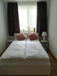 1 cama blanca con 2 almohadas frente a una ventana en APARTAMENT RELAX, en Ełk