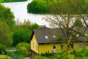 ein gelbes Haus mit einem See im Hintergrund in der Unterkunft Isaan Ostrzyce - Samodzielne Apartamenty i Tajska Kuchnia in Ostrzyce