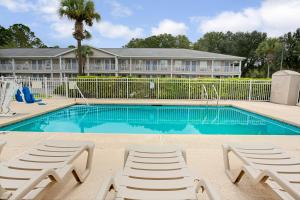 a swimming pool with two lounge chairs in front of a building at Travelodge Suites by Wyndham MacClenny I-10 in Macclenny