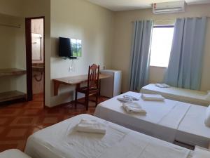 a hotel room with two beds and a desk and a television at Hotel Litoral in Aracaju