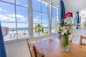 een vaas met bloemen op een tafel in een kamer met ramen bij Vista Mar Apartamentos in Puerto del Carmen