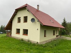 a house with a red roof on a green field at Chalupa u Bártů in Trojanovice