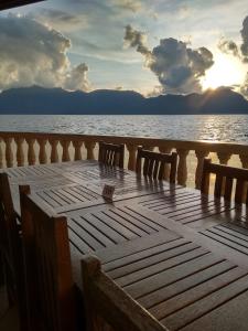 a wooden table with two chairs on a deck overlooking the water at Hotel Maninjau Indah - The Lakeside Resort in Maninjau