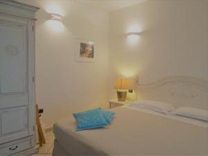 a white bedroom with a bed with a blue pillow on it at Hotel Mariposas in Villasimius