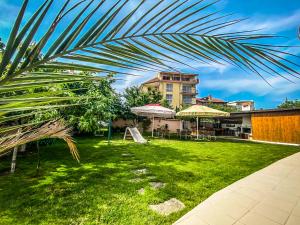 a green yard with tables and umbrellas and a building at Vanessa Family Hotel in Ravda