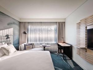 a bedroom with a bed and a desk and a window at Novotel Tainui Hamilton in Hamilton