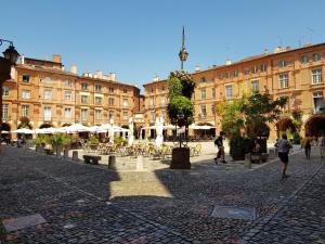una calle de la ciudad con mesas, sillas y edificios en La parenthèse gourmande avec clim et parking, en Montauban