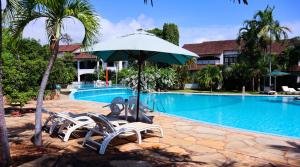 un grupo de sillas y una sombrilla junto a la piscina en Woburn Residence Club Apartments, en Malindi