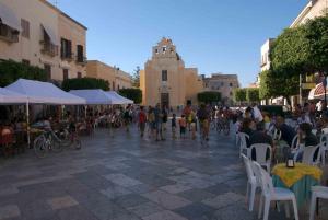 una folla di persone che camminano per strada con tavoli e sedie di Il Ritrovo di Archimede a Favignana