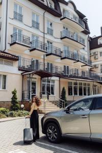 Una donna in piedi accanto a un'auto di fronte a un edificio. di Nota Bene Hotel & Restaurant a Lviv