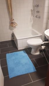 y baño con aseo, bañera y alfombra azul. en Meerblick, en Glücksburg