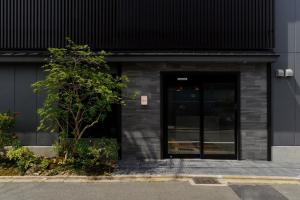 ein schwarzes Gebäude mit einer Tür und einem Baum in der Unterkunft ikoi HOTEL in Kyoto