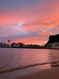 un tramonto su una spiaggia con un corpo d'acqua di Apartamentos La Puntilla Mogan a Puerto de Mogán