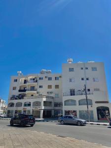 Deux voitures garées devant un grand bâtiment dans l'établissement Pearl City View Apartment, à Paphos