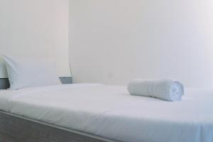 a white bed with a rolled up towel on it at Lavish 2BR Apartment at Grand Sungkono Lagoon By Travelio in Surabaya