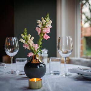 a vase with flowers in it on a table with glasses at Blakeney House in Blakeney