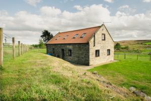a small stone building with a red roof on a field at The Old Cow Byre in Lealholm