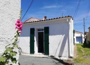 een klein wit gebouw met groene deuren en een bloem bij La Marinière, 3chb, à 500m de la mer - St Denis Oléron in La Gautrie