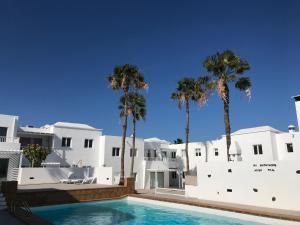 una piscina di fronte a un edificio bianco con palme di Romantic Casa Blanca a Costa Teguise