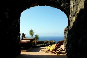 an arch in a stone wall with chairs and the ocean at Dammusi di Sofia in Pantelleria +10 photos