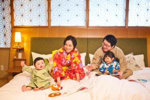 una familia sentada en una cama con dos bebés en Honjin Hiranoya Kachoan en Takayama