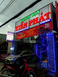 une voiture garée devant un restaurant avec des panneaux de néons dans l'établissement KHÁCH SẠN TIẾN PHÁT, à Cà Mau